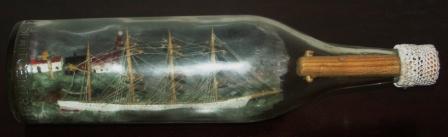 20th century ship model housed in bottle with decorative ropework. Signed "Skillinge March 4th 1973" and depicting a Swedish 4-masted barque in front of a lighthouse and lightkeeper houses. 