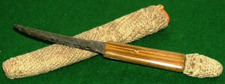 Knife with decorative steel-blade, wooden handle and rope-coated leather sheath.