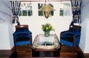 Part of a domestic livingroom furnished with restored 20th century original ship's easy chairs and porthole table as well as newly made brass lamp.