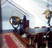 Part of a domestic diningroom furnished with restored 20th century original ship's table, swivel chairs, bureau, original deck-planking and original brass search light with bilt in TV-set as well as newly made brass ceiling lamp.