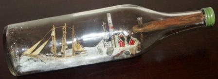 Early 20th century sailor-made ship model housed in bottle. Depicting a Swedish 3-masted barque with lighthouse and lightkeeper houses. 